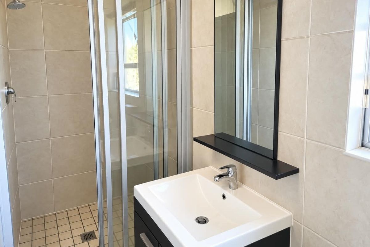 A clean, modern bathroom featuring a glass-enclosed shower, a contemporary vanity with a basin, and neutral wall tiling.