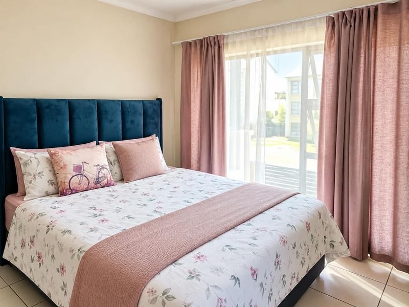 A well-lit bedroom featuring tiled flooring and a large sliding glass door with curtain tracks, providing natural light and access to the exterior.