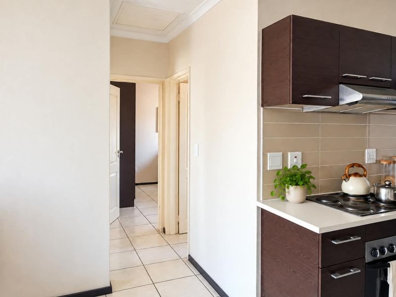 A functional kitchen area featuring dark wood cabinetry, a tiled backsplash, and integrated cooking appliances, leading into a tiled hallway.