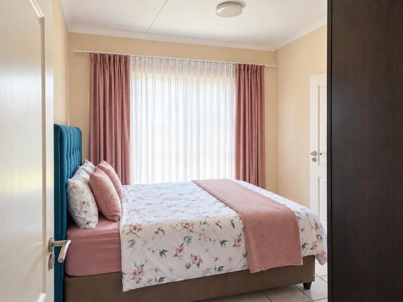 A well-maintained bedroom featuring neutral wall tones, tiled flooring, and a large window dressed with curtains.