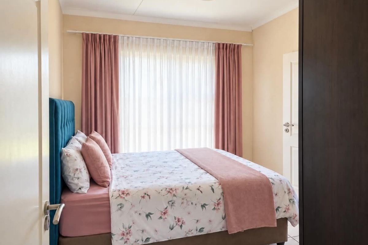 A well-maintained bedroom featuring neutral wall tones, tiled flooring, and a large window dressed with curtains.