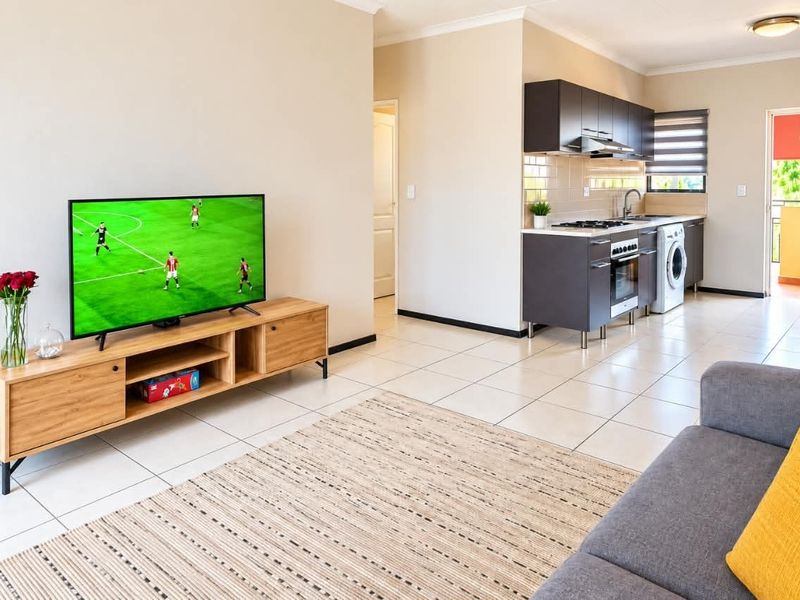 An open-plan living area featuring tiled floors and a modern kitchen with built-in cabinetry, oven, hob, and extractor fan, leading to a balcony.