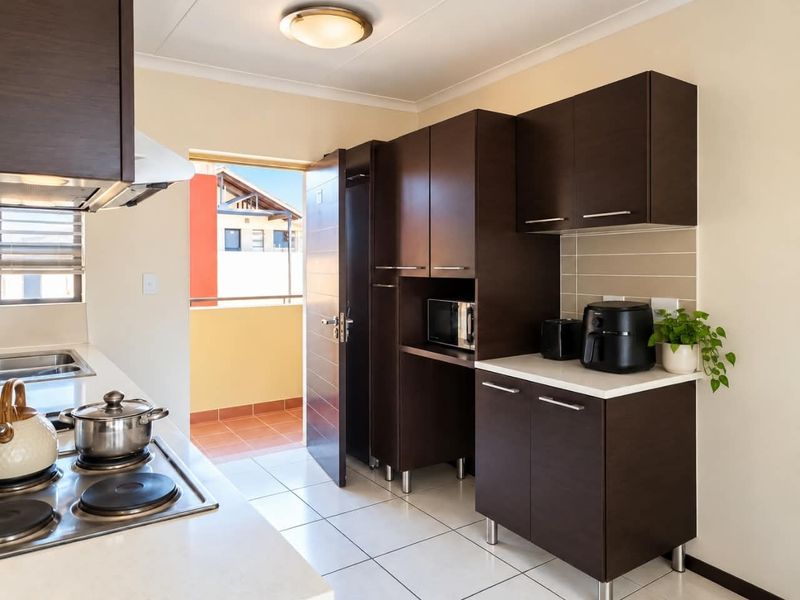 Modern kitchen featuring dark wood cabinetry, tiled flooring, built-in electric hob, and direct access to a private balcony.