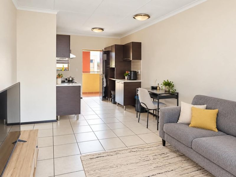 An open-plan living and kitchen area featuring tiled flooring, modern dark cabinetry, and direct access to a balcony.