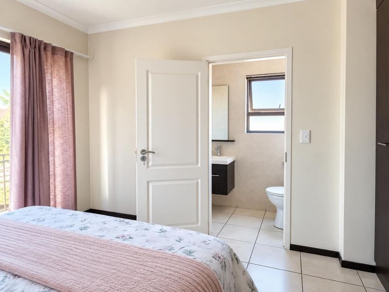 A well-lit bedroom featuring neutral tones, tiled flooring, and direct access to a private en-suite bathroom with modern fixtures.