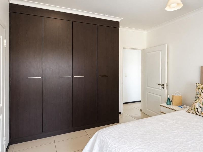 A well-maintained bedroom featuring dark wood built-in cupboards, neutral tiled flooring, and clean white walls.