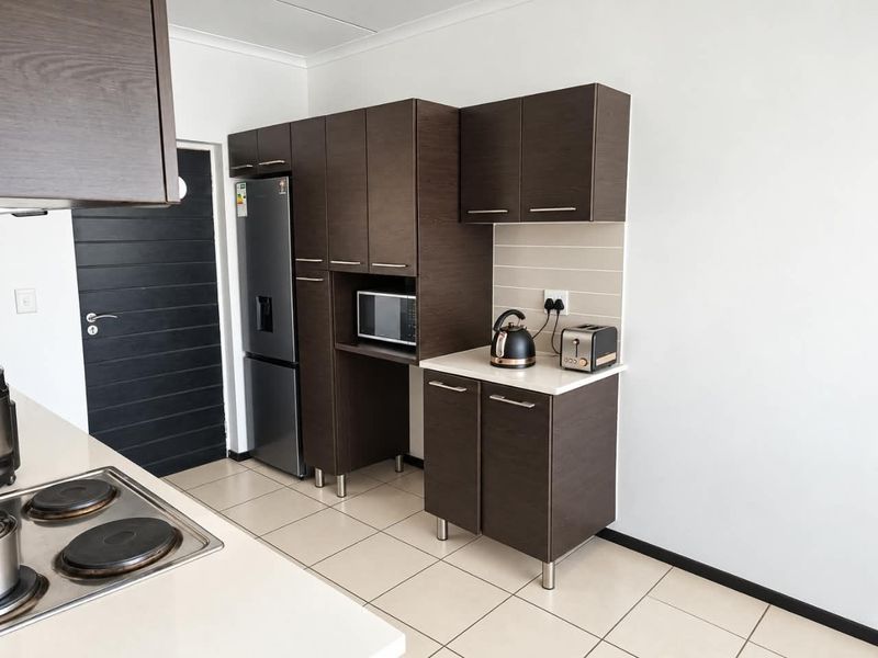 Modern kitchen featuring dark wood-grain cabinetry, stone countertops, tiled splashback, and integrated electric hob with ample storage space.