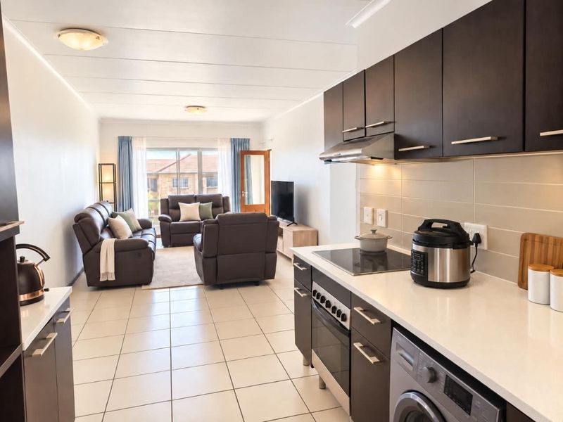 Modern open-plan living area featuring a contemporary kitchen with dark cabinetry, stone countertops, and integrated appliances, flowing into a bright, tiled lounge space.