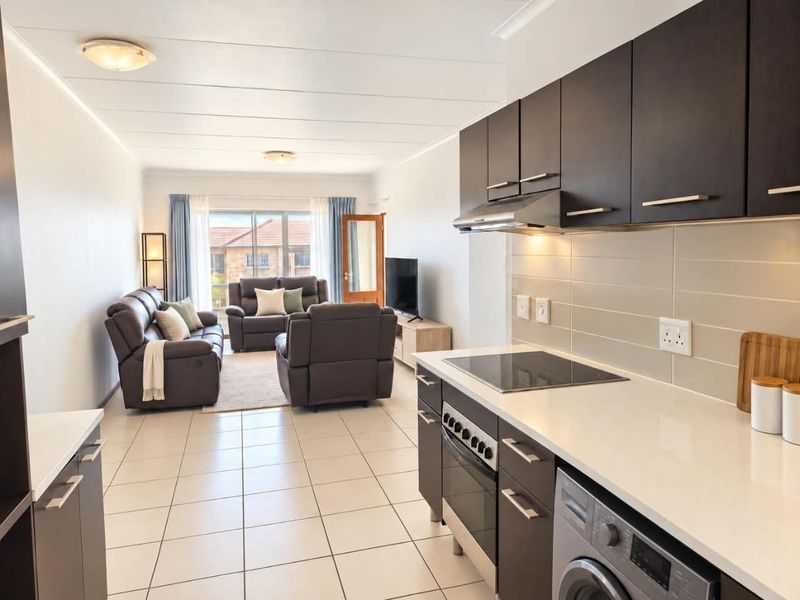 Modern open-plan living area featuring a well-equipped kitchen with dark cabinetry, stone countertops, and integrated appliances, flowing into a comfortable lounge space.