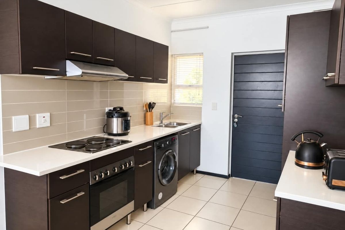 Modern kitchen featuring dark cabinetry, white countertops, tiled splashback, built-in oven with hob, extractor fan, and integrated laundry appliance.