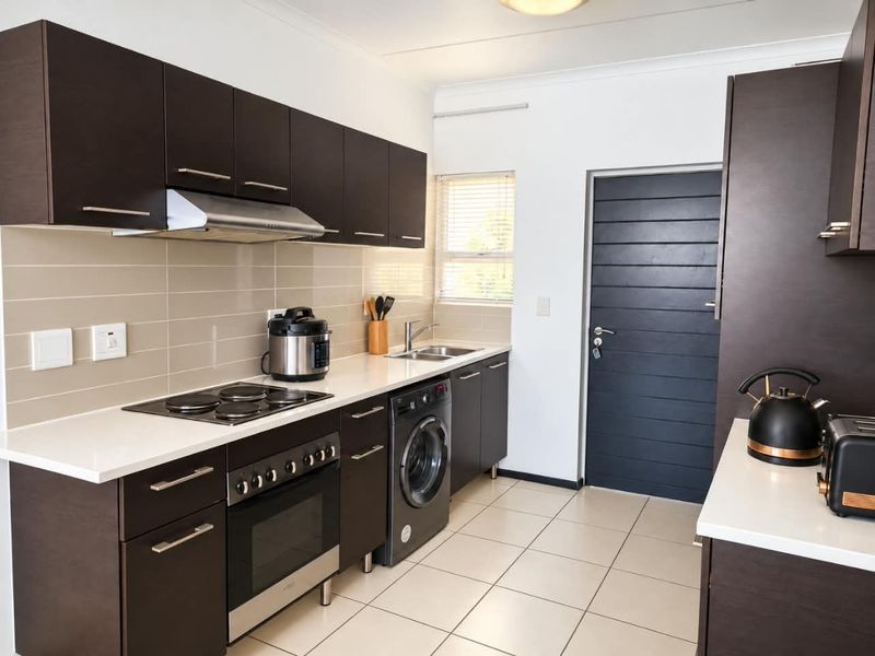 Modern kitchen featuring dark cabinetry, white countertops, tiled splashback, built-in oven with hob, extractor fan, and integrated laundry appliance.