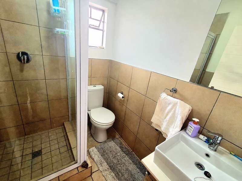 A functional bathroom featuring a glass-enclosed shower, a wall-mounted vanity basin with a mixer tap, and neutral wall tiling.
