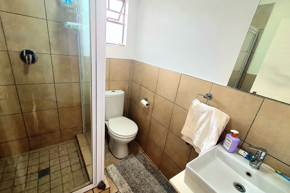 A functional bathroom featuring a glass-enclosed shower, a wall-mounted vanity basin with a mixer tap, and neutral wall tiling.