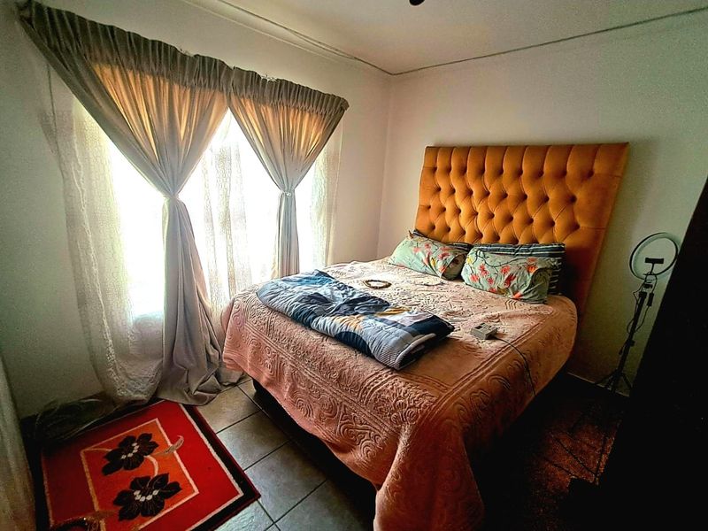 A bedroom featuring tiled flooring and natural light through a window with curtain rails.
