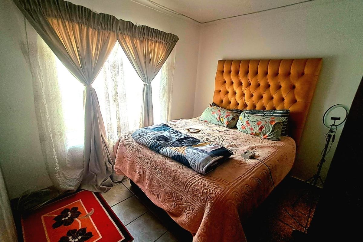 A bedroom featuring tiled flooring and natural light through a window with curtain rails.