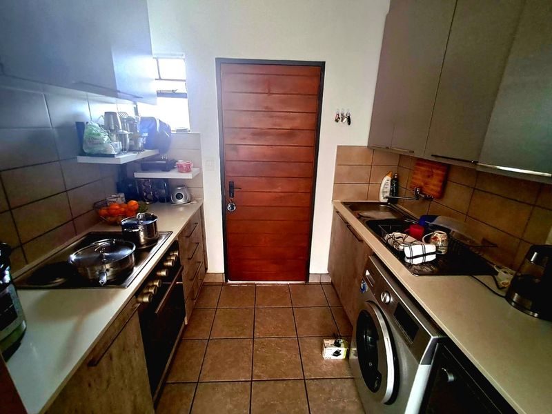 A functional galley-style kitchen featuring built-in cabinetry, integrated oven and hob, tiled backsplash, and dedicated laundry plumbing connections.