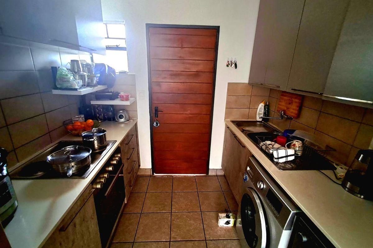 A functional galley-style kitchen featuring built-in cabinetry, integrated oven and hob, tiled backsplash, and dedicated laundry plumbing connections.