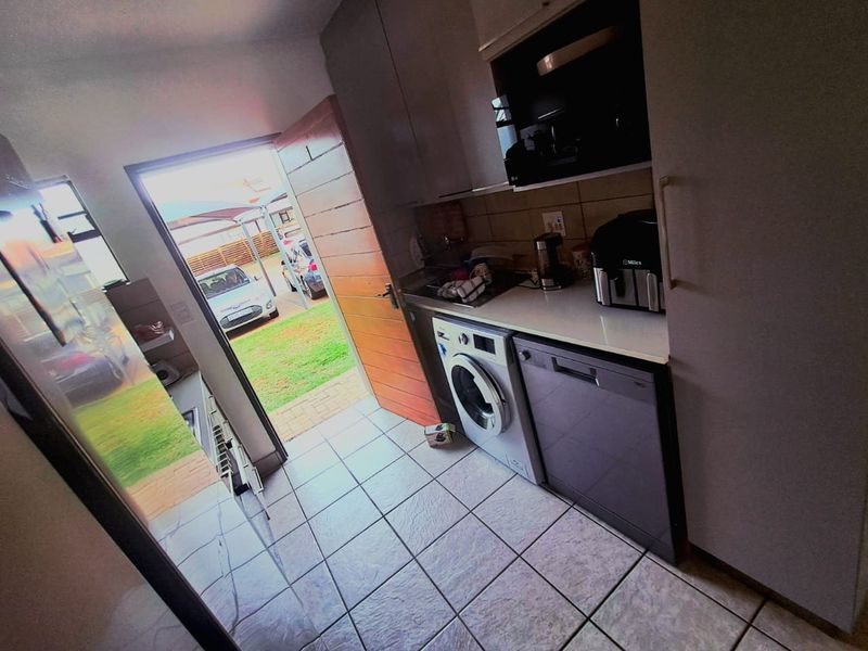 Compact kitchen featuring built-in cabinetry, tiled flooring, and integrated laundry and dishwasher appliances, with direct access to the exterior.