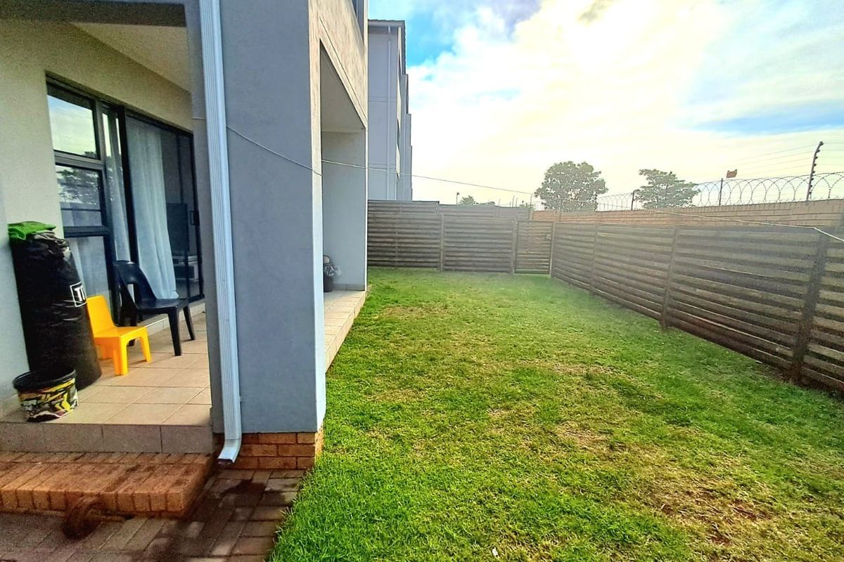 A private rear garden featuring a paved patio area, a well-maintained lawn, and secure perimeter fencing with integrated security measures.