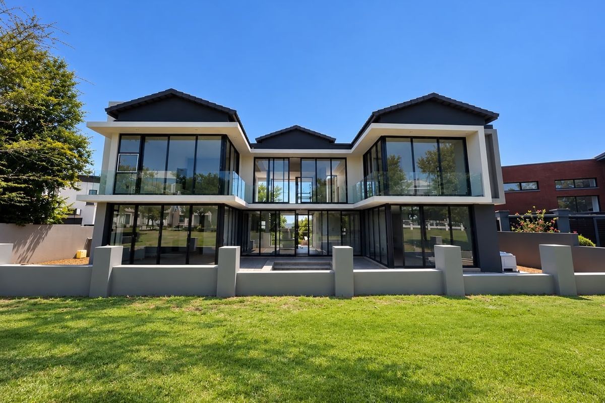 Modern double-story residence featuring extensive glass facades, sleek architectural lines, and a well-maintained rear garden with a paved patio area.
