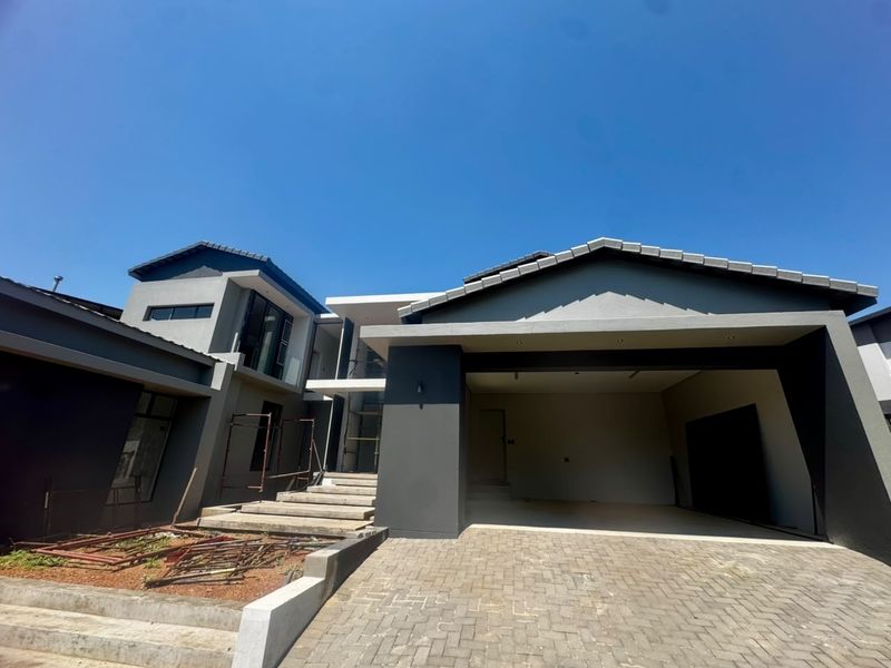 Modern contemporary house exterior featuring a paved driveway, double garage, and concrete entrance steps, currently undergoing final landscaping and finishing touches.