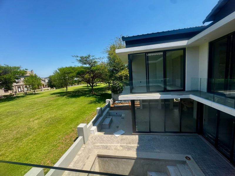 Rear view of a modern double-story home featuring large sliding glass doors, a glass balustrade, and an unfinished patio and pool area.