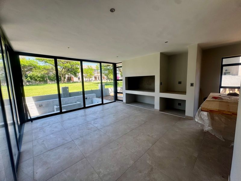 Modern open-plan living area featuring large format floor tiles, a built-in fireplace, and expansive floor-to-ceiling sliding doors with views of the garden.