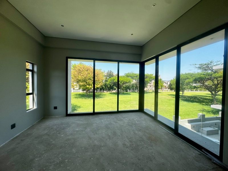 A spacious, empty living area featuring large floor-to-ceiling sliding glass doors that provide abundant natural light and views of the garden.