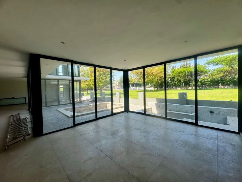 Spacious, modern living area featuring large format floor tiles and expansive floor-to-ceiling sliding doors with views of the garden and pool area.