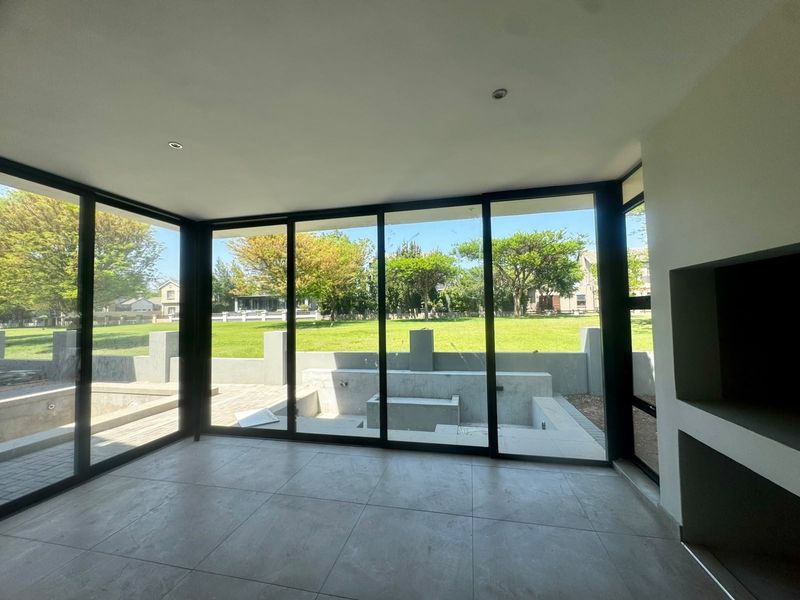 Modern living area featuring large format floor tiles, a built-in fireplace, and expansive black aluminium sliding doors opening to a landscaped garden.