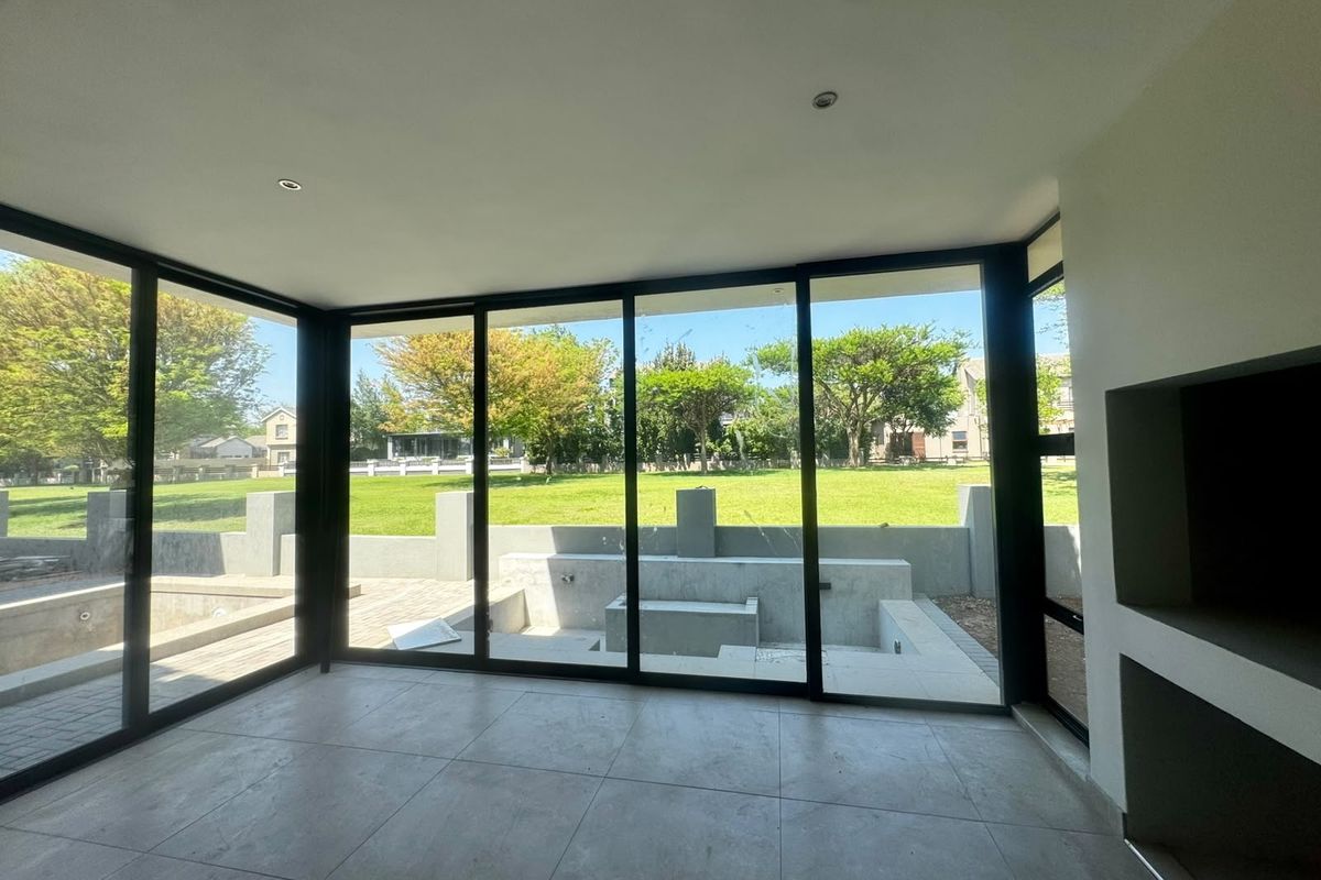 Modern living area featuring large format floor tiles, a built-in fireplace, and expansive black aluminium sliding doors opening to a landscaped garden.