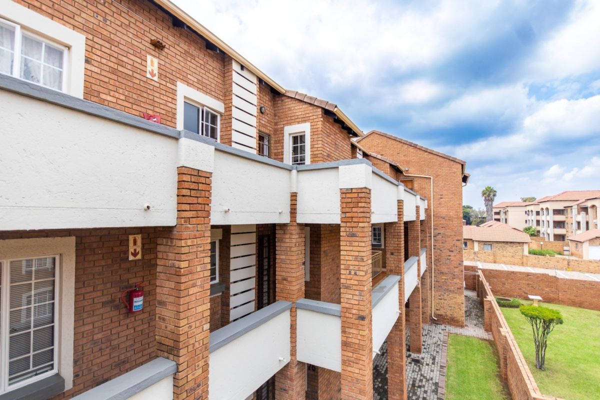 Exterior view of a multi-story face brick apartment building featuring private balconies, paved walkways, and a well-maintained communal garden area.