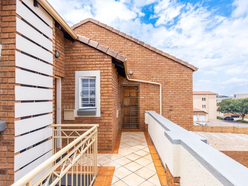 A private balcony featuring brick exterior walls, tiled flooring, and a secure metal balustrade overlooking the surrounding complex area.
