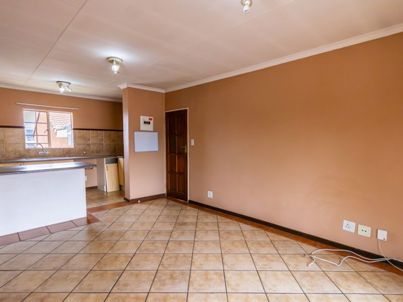 An open-plan living and kitchen area featuring tiled flooring, neutral wall tones, and functional kitchen cabinetry with a breakfast counter.