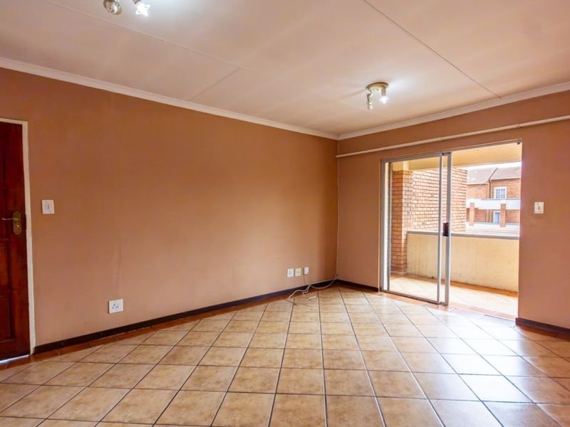 An empty living room featuring tiled flooring, neutral wall paint, and a sliding glass door providing access to an outdoor balcony area.