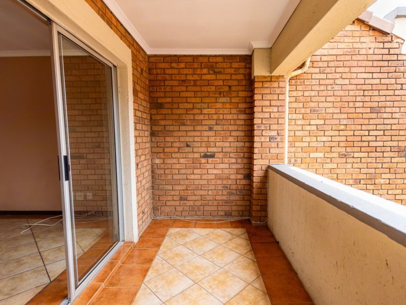 A covered balcony featuring exposed brick walls, tiled flooring, and a sliding glass door providing access to the interior living space.
