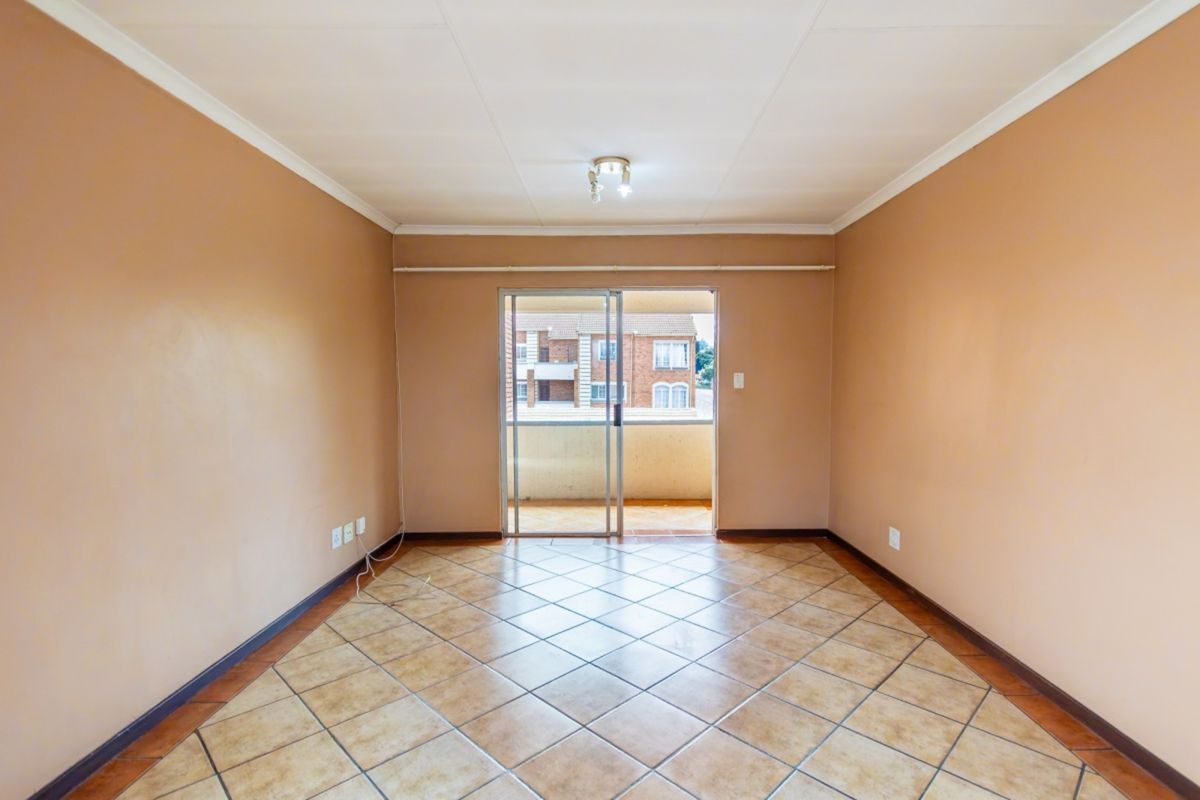 An empty living room featuring tiled flooring, neutral walls, and a sliding glass door providing access to an outdoor balcony area.