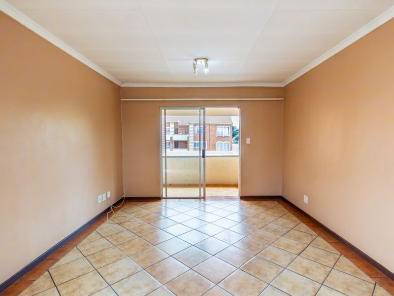 An empty living room featuring tiled flooring, neutral walls, and a sliding glass door providing access to an outdoor balcony area.