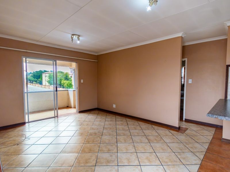 An open-plan living area featuring tiled flooring, neutral wall tones, and a sliding glass door providing access to an outdoor balcony space.