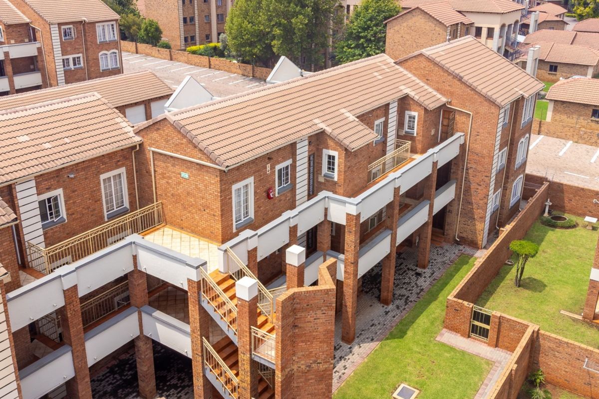 Aerial view of a multi-story residential flat complex featuring face brick architecture, tiled roofs, external staircases, and well-maintained communal garden areas.