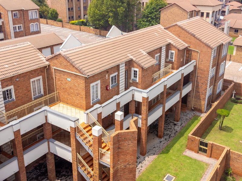 Aerial view of a multi-story residential flat complex featuring face brick architecture, tiled roofs, external staircases, and well-maintained communal garden areas.