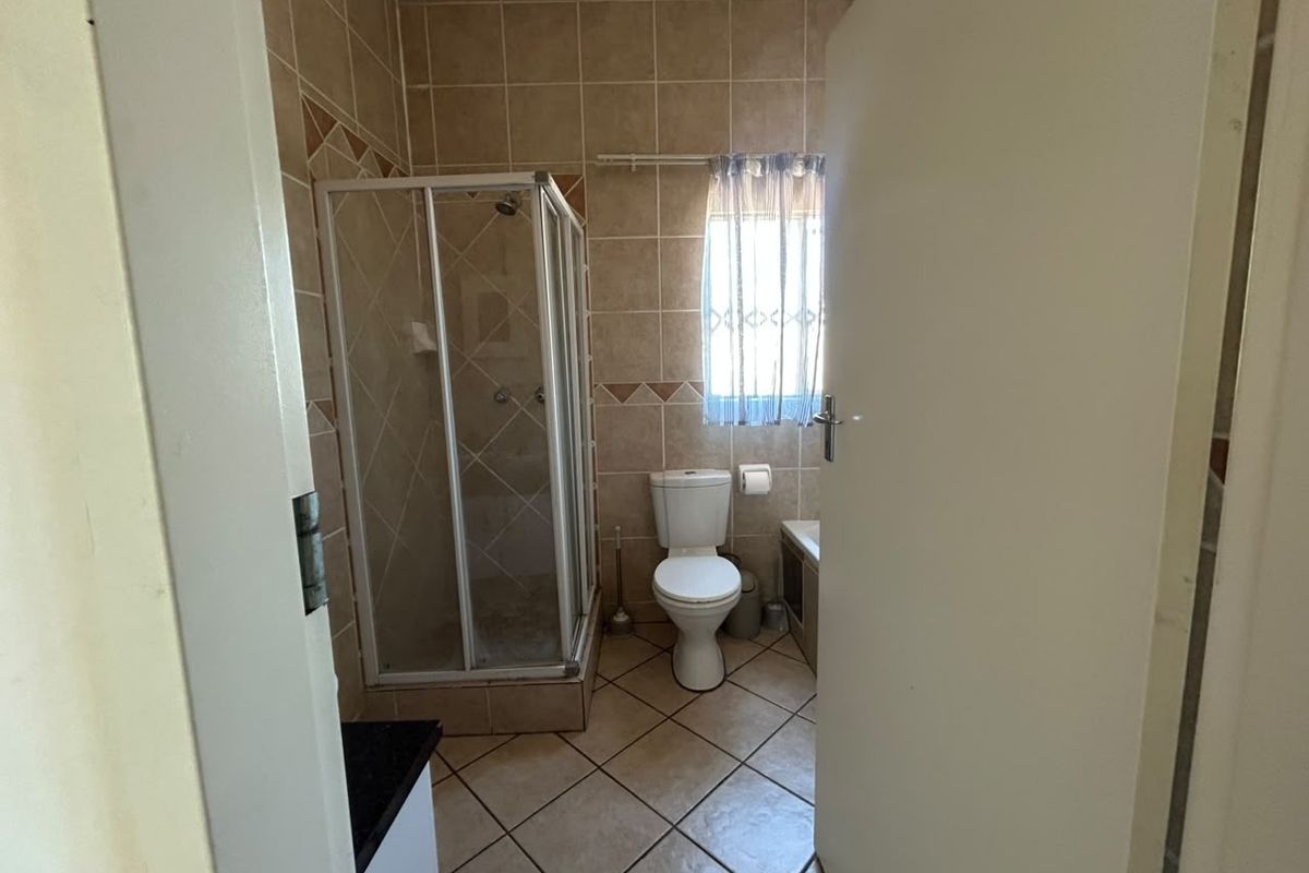 A functional bathroom featuring a shower enclosure, toilet, and neutral tiled finishes throughout, offering a practical layout for a townhouse property.
