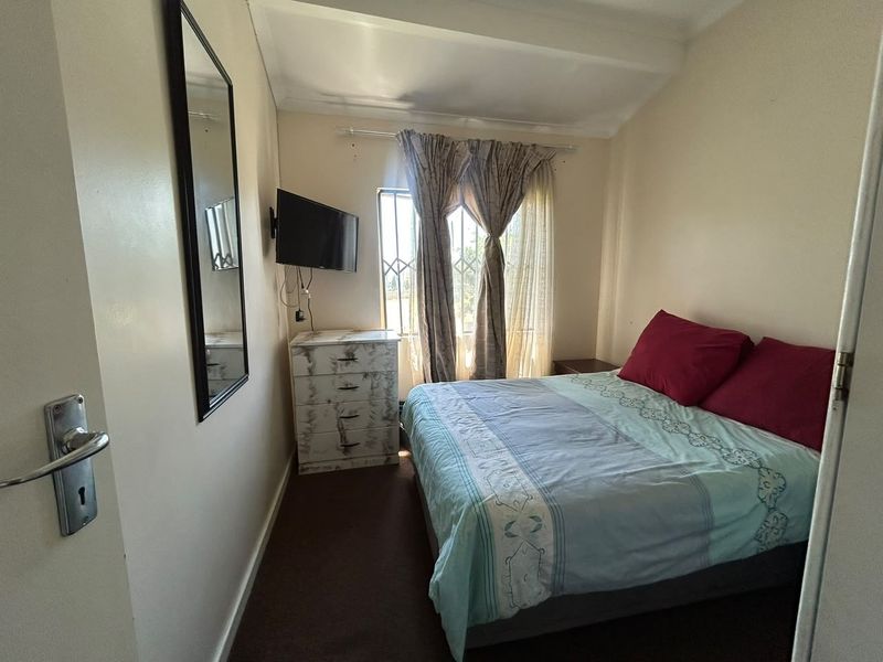 A compact bedroom featuring a window with security bars, neutral wall finishes, and carpeted flooring.