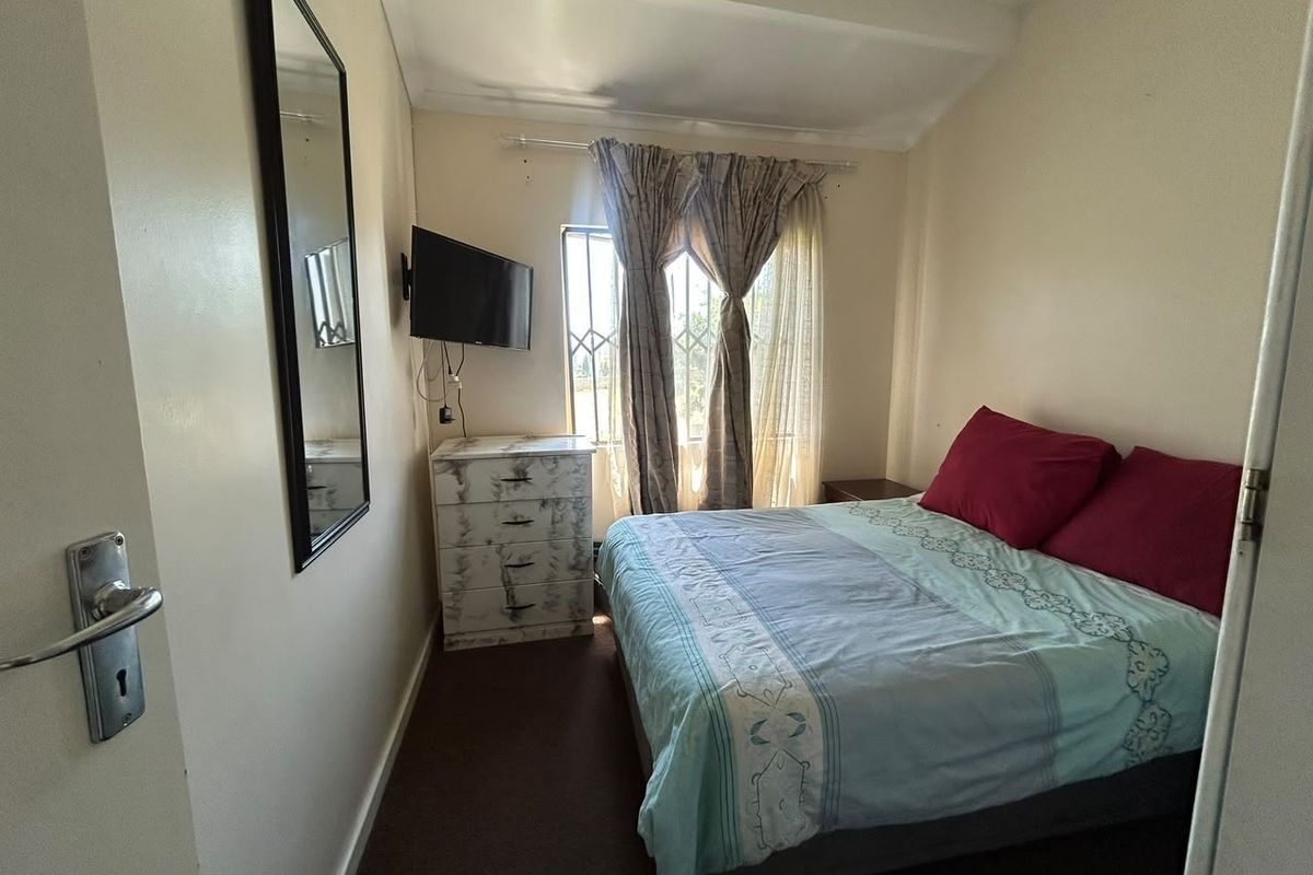 A compact bedroom featuring a window with security bars, neutral wall finishes, and carpeted flooring.