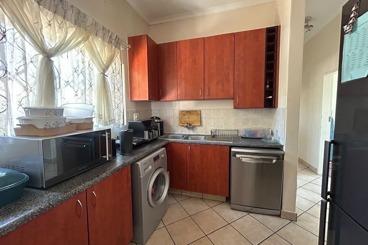 Functional kitchen featuring warm-toned laminate cabinetry, granite countertops, tiled backsplash, and dedicated spaces for a dishwasher and washing machine.