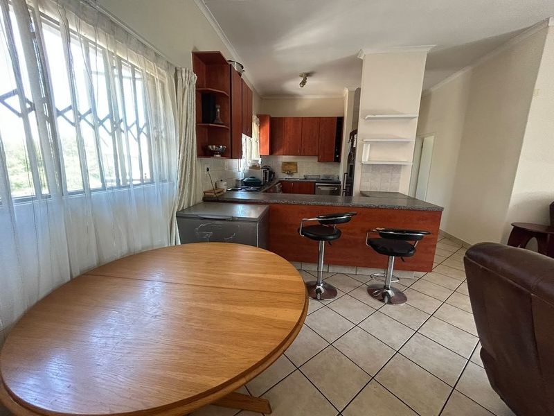 Open-plan kitchen and dining area featuring tiled flooring, built-in wooden cabinetry, and a breakfast bar, offering a functional layout for daily living.