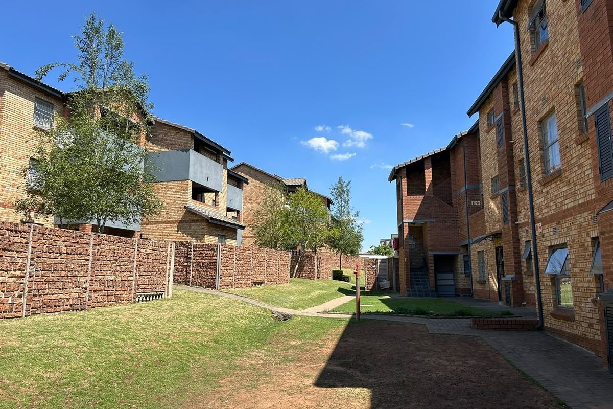 A view of the apartment complex exterior featuring face brick buildings, paved walkways, and well-maintained communal garden areas.