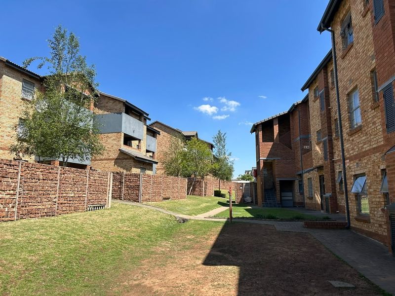 A view of the apartment complex exterior featuring face brick buildings, paved walkways, and well-maintained communal garden areas.