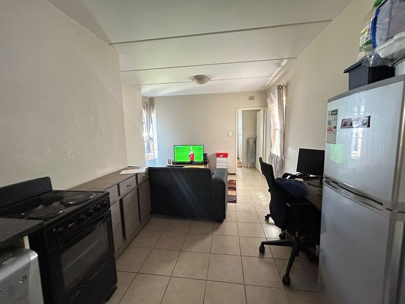 Open plan living area featuring tiled flooring and a functional kitchen space with built-in cabinetry and an electric stove.