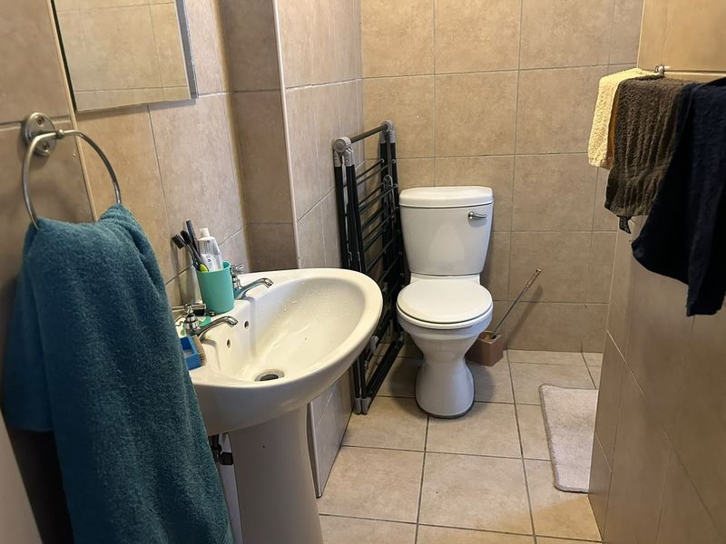 A functional bathroom featuring a pedestal washbasin, toilet, and neutral ceramic tiling throughout.